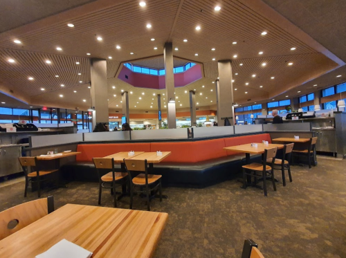 Interior of a modern restaurant featuring wooden tables, red and black seating, and large windows with ambient lighting.