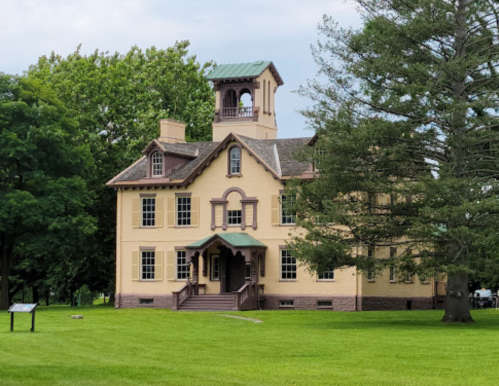 Historic yellow building with a bell tower, surrounded by green trees and grass.