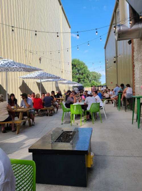 Outdoor dining area with tables, umbrellas, and string lights, filled with people enjoying a sunny day.