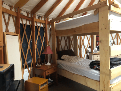 Interior of a cozy yurt with a bunk bed, wooden furniture, and warm lighting.