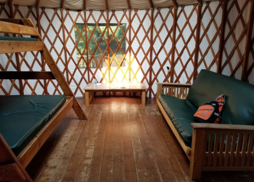 Interior of a yurt featuring a bunk bed, a sofa, a wooden table, and a window with natural light.