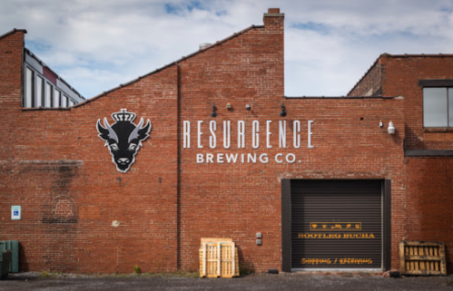 Brick wall of Resurgence Brewing Co. featuring a logo of a deer head and a loading dock with wooden pallets.