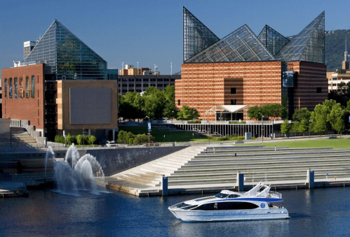 A modern building with glass architecture beside a river, featuring a boat and landscaped steps along the water's edge.