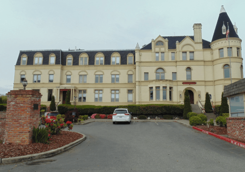Historic building with a turret, surrounded by landscaped gardens and a parking area.