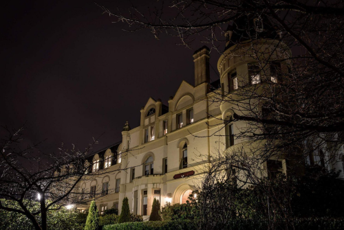 A grand, illuminated building at night, surrounded by dark trees and a cloudy sky.