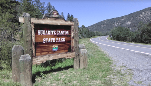 Sign for Sugarite Canyon State Park beside a winding road, surrounded by green hills and clear blue sky.