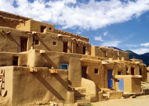 Adobe buildings with blue doors under a bright sky, showcasing traditional Pueblo architecture.