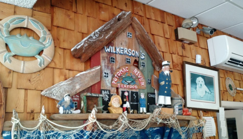 A rustic seafood restaurant interior featuring a wooden sign, nautical decor, and figurines on a shelf.