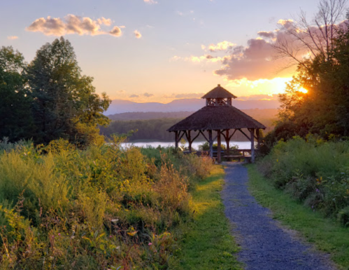 A scenic path leads to a gazebo at sunset, surrounded by lush greenery and mountains in the background.