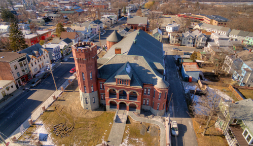Aerial view of a historic brick building with a tower, surrounded by residential streets and snow-covered ground.