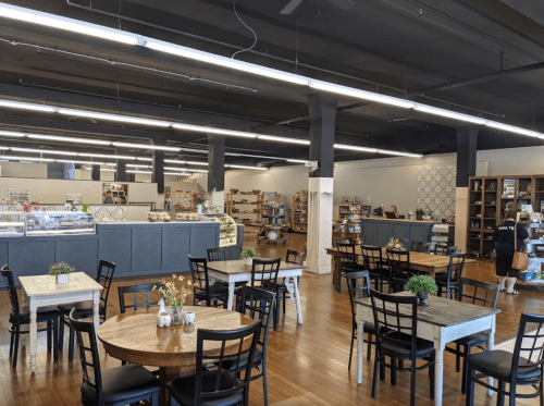 A spacious café with wooden tables, chairs, and a display case filled with pastries, featuring a modern, bright interior.