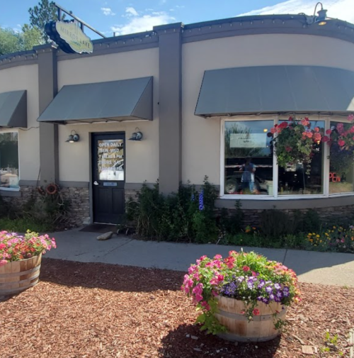 A charming storefront with flower planters, featuring a sign that says "Open Daily" and large windows with plants.