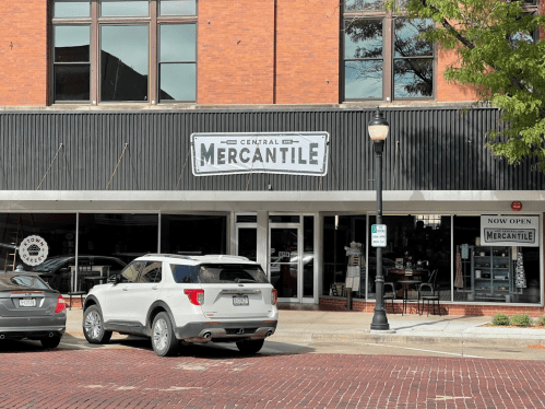 A storefront with a sign reading "Central Mercantile," featuring large windows and a white SUV parked outside.