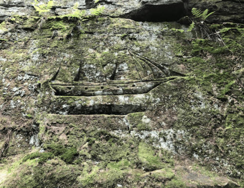 Carved ship design on a moss-covered rock face, surrounded by greenery.