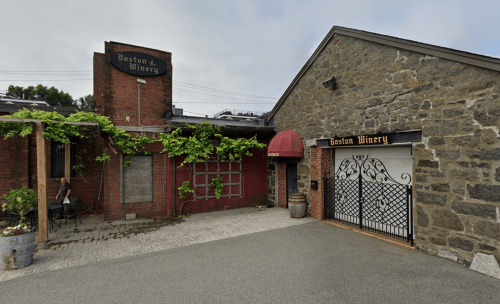 Exterior view of Boston Winery, featuring brick walls, a gated entrance, and greenery along the building.