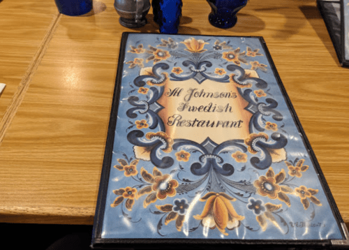 A decorative menu for "Al Johnson's Swedish Restaurant" on a wooden table, featuring floral designs.