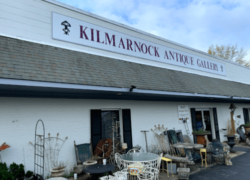 Exterior of Kilmarnock Antique Gallery, featuring a sign and various antique items displayed outside.