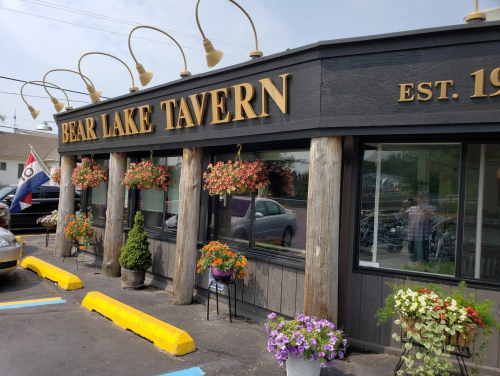 Exterior of Bear Lake Tavern with flower planters, wooden pillars, and a sign displaying "EST. 1990."