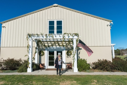A woman walks towards a large, light-colored barn with an American flag and greenery adorning the entrance.