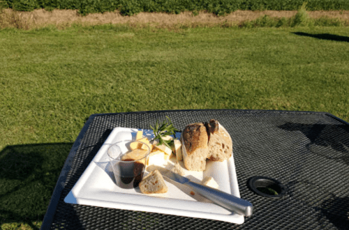 A plate with assorted bread, cheese, and a small cup of sauce, set on a table in a grassy outdoor area.
