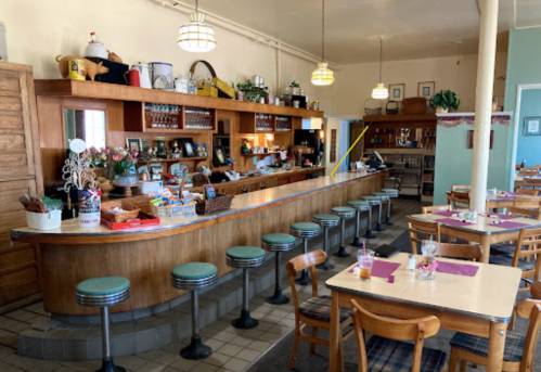 A cozy diner interior featuring a wooden counter, bar stools, and tables set with purple napkins. Vintage decor adorns the walls.