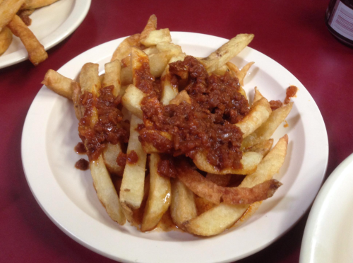 A plate of French fries topped with a hearty chili sauce, served on a red table.