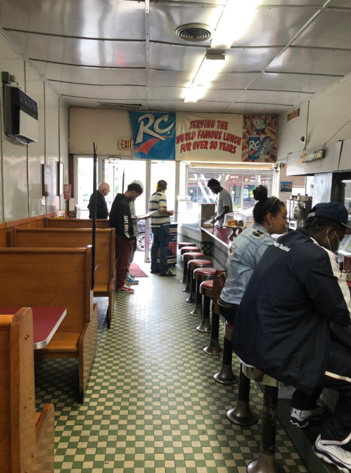 A diner interior with patrons at the counter and tables, featuring a vintage decor and a sign about its famous lunch.