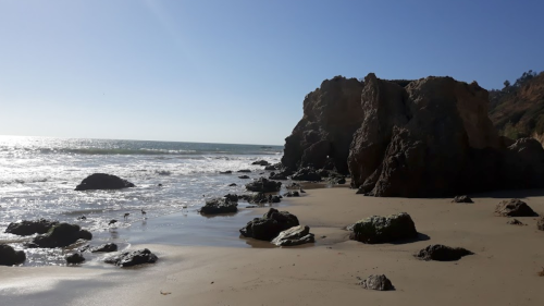 A serene beach scene with rocky formations, gentle waves, and clear blue skies.