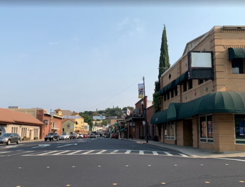 A quiet street scene featuring brick buildings, green awnings, and a clear sky in a small town.