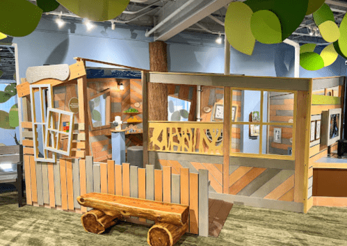 A colorful children's play area featuring wooden structures, a tree, and a bench, designed for imaginative play.