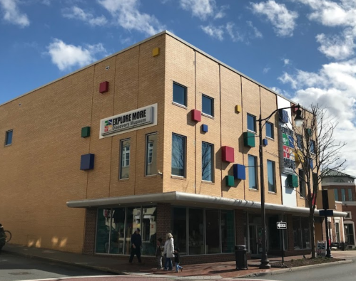 A modern yellow building with colorful square accents and large windows, under a partly cloudy sky.