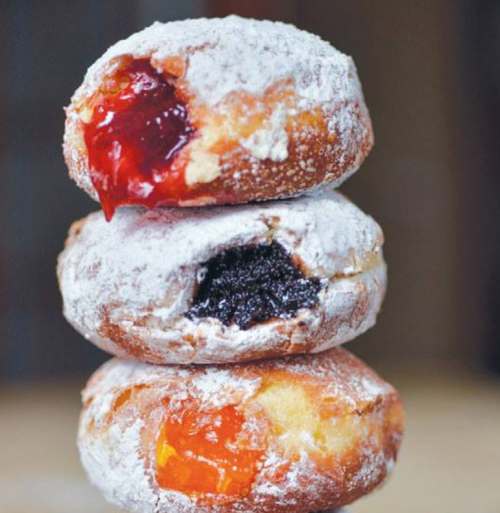 Three powdered sugar donuts stacked, filled with red jam, dark chocolate, and orange filling.