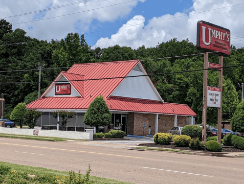 A restaurant with a red roof and sign, surrounded by greenery and a clear blue sky.
