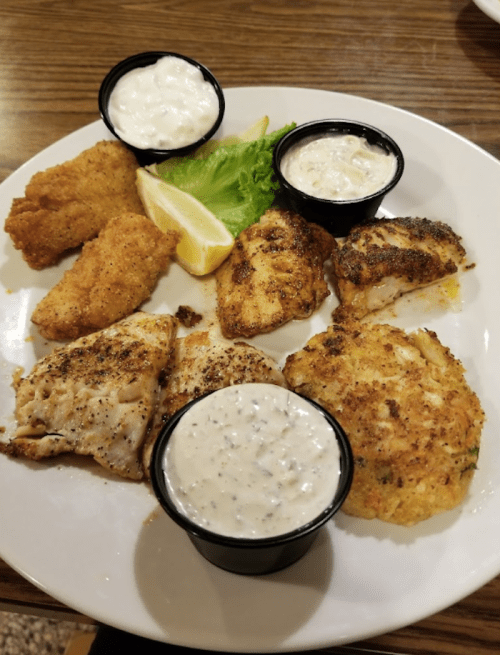 A plate of assorted fried fish, crab cakes, and dipping sauces, garnished with lettuce and lemon wedges.