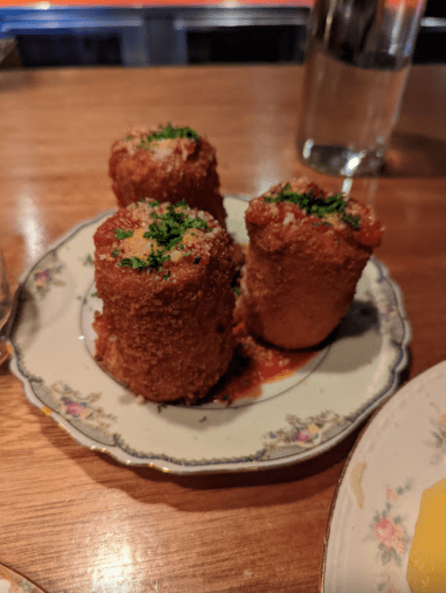 Three crispy, breaded rolls topped with herbs on a decorative plate, served with a red sauce.