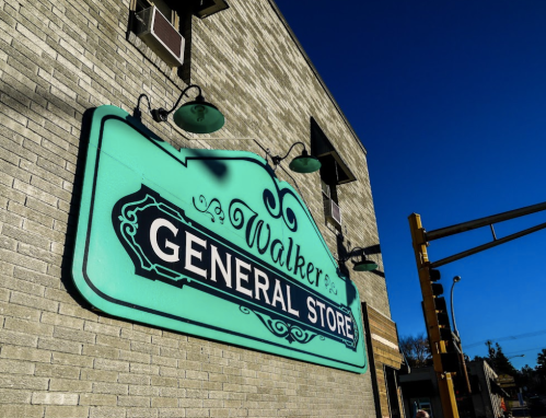 Sign for "Walker’s General Store" in a vintage style, mounted on a brick wall under a clear blue sky.