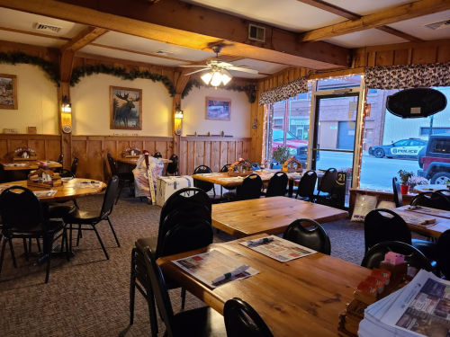 Cozy restaurant interior with wooden decor, tables set for dining, and large windows showing a street view.