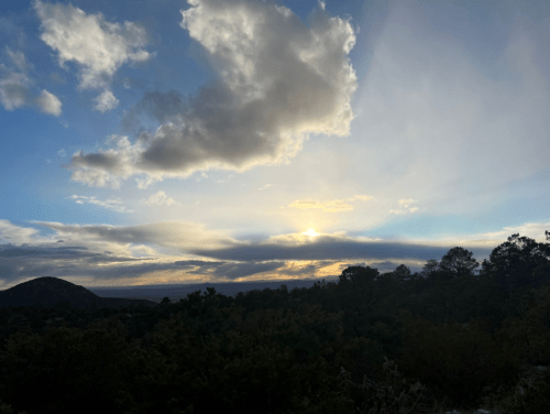 A scenic view of a sunset with clouds and mountains, casting a warm glow over the landscape.