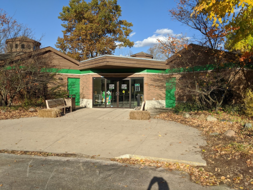 Entrance of a building with green accents, surrounded by trees and autumn foliage, on a clear day.