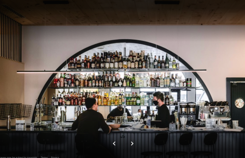 A modern bar with a curved shelf filled with various bottles, two bartenders working behind the counter.