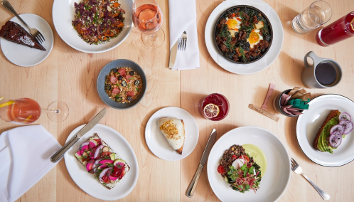 A table spread with various colorful dishes, including salads, eggs, and desserts, alongside drinks and utensils.