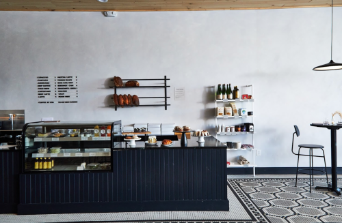A modern café interior featuring a display case, shelves of products, and a small table with a chair.