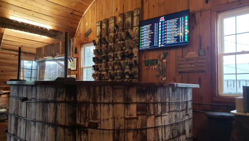 A rustic wooden bar with a menu display on the wall and a collection of mugs hanging nearby.