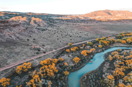 Aerial view of a winding river surrounded by autumn-colored trees and rugged terrain under a clear sky.