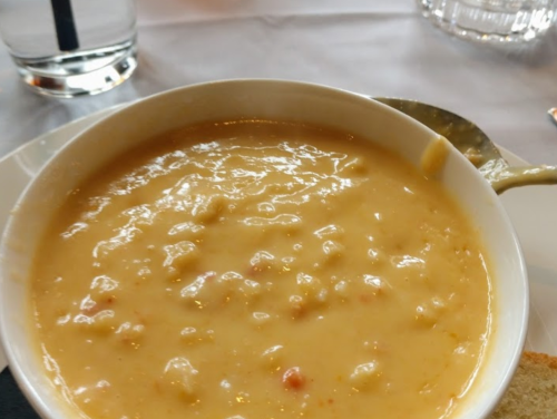 A bowl of creamy soup with a smooth texture, served on a white plate with a spoon beside it.