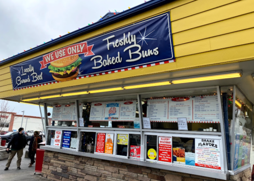 A colorful fast-food stand with a menu, featuring freshly baked buns and various food options.