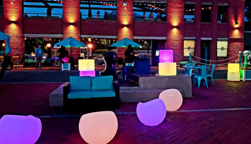 Colorful illuminated furniture and seating in an outdoor space with a lively atmosphere and people in the background.