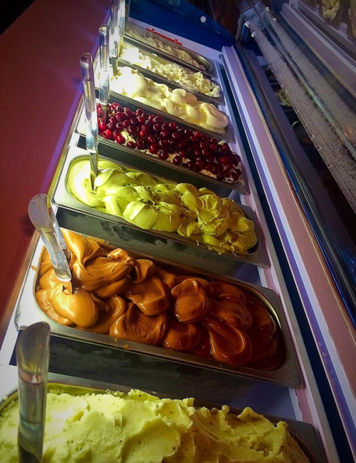 A variety of colorful gelato flavors displayed in metal tubs, with spoons for serving.