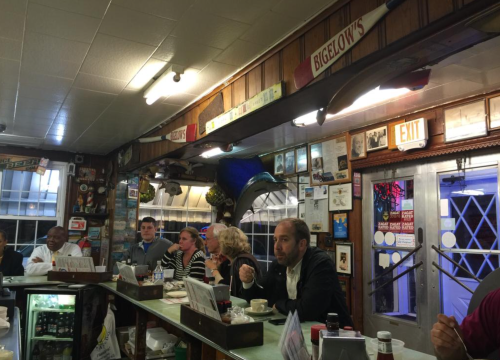 A cozy diner scene with patrons at the counter, vintage decor, and a blue marlin mounted on the wall.