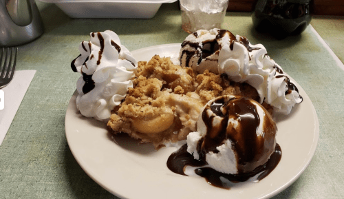 A plate with apple crisp topped with whipped cream and two scoops of ice cream drizzled with chocolate sauce.